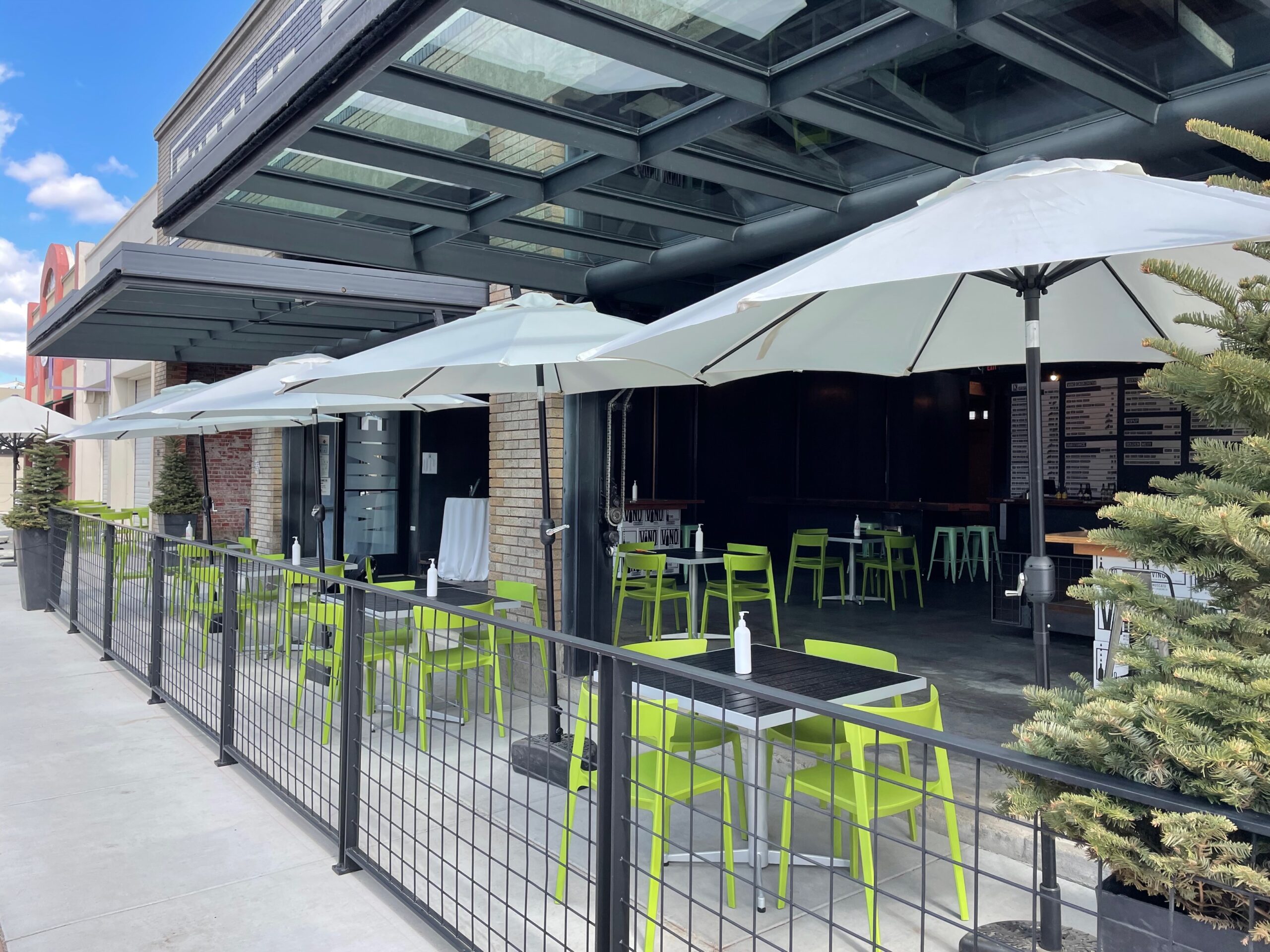 A view from the front of our Walla Walla Downtown tasting room. Showing blue sky, the garage door open, and tables ouside/inside ready for wine tasting.